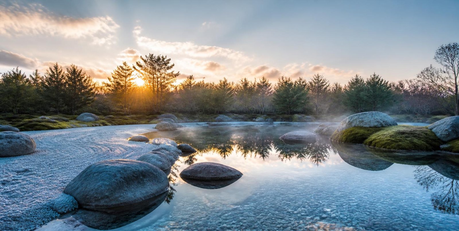 Raked gravel and smooth stones beside a clear, still pool at sunrise, pink clouds reflected in the water